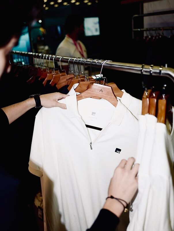 Cliente escolhendo uma camisa polo branca numa arara de roupas da Aramis