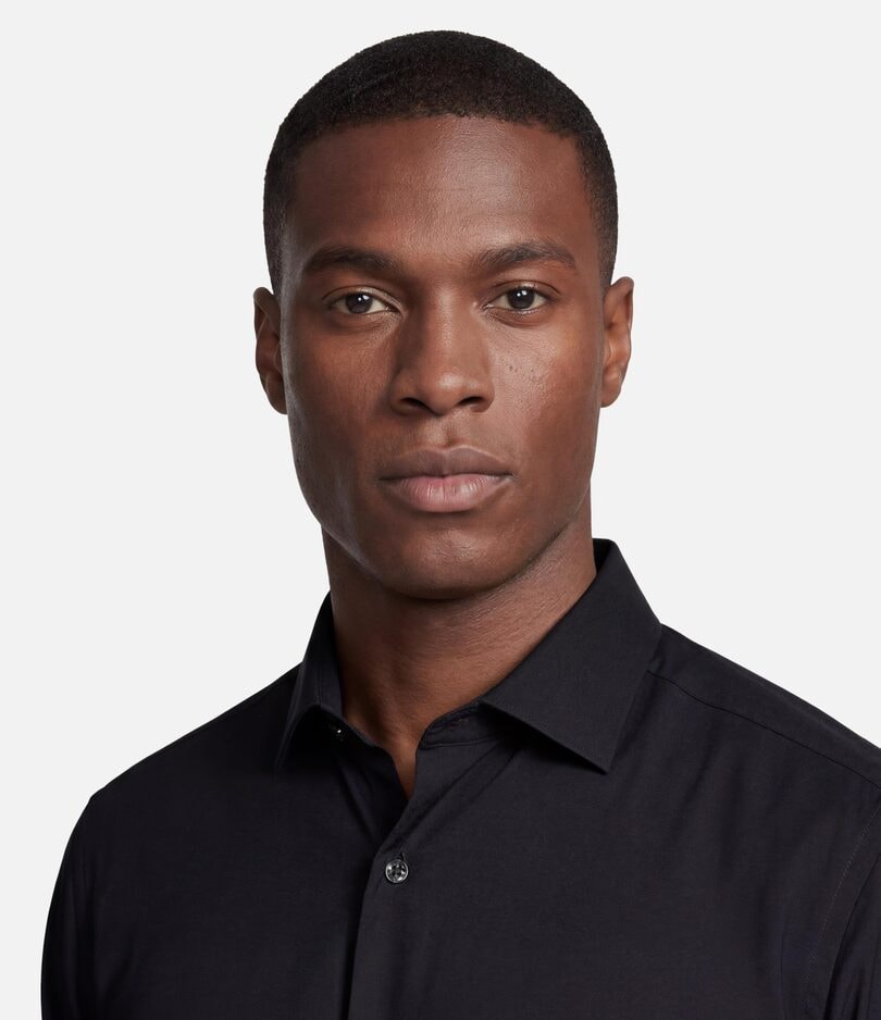 Retrato de homem de camisa social preta olhando para a câmera, em fundo de estúdio cinza claro